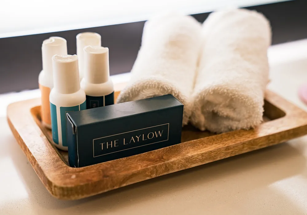 Wooden tray holding amenity bottles and rolled towels in a hotel bathroom.
